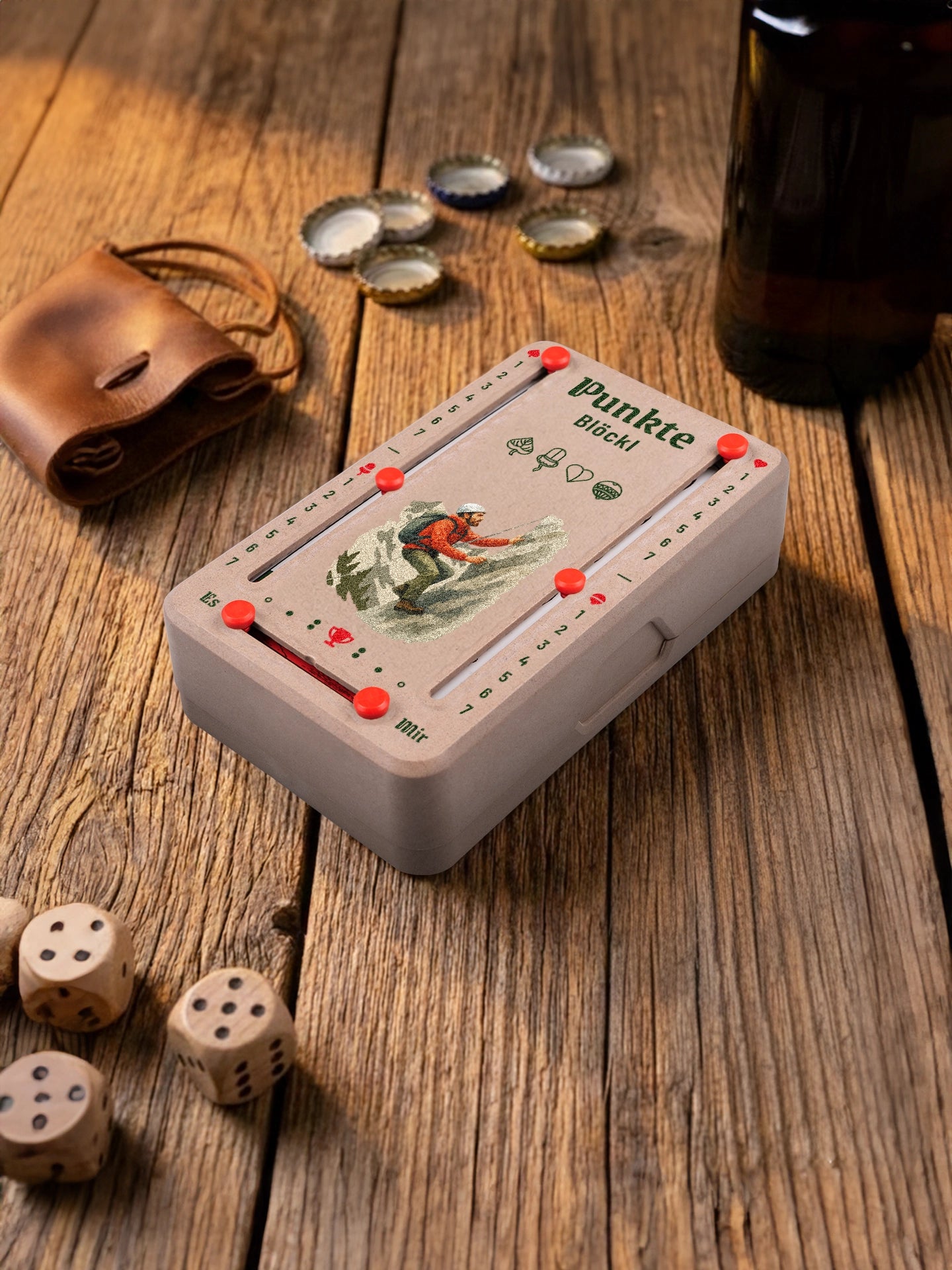 Punkteblöckl in Holzoptik mit roten Pins und Bergsteigen-Motiv. Platziert auf Holztisch mit Würfeln und Kronkorken.